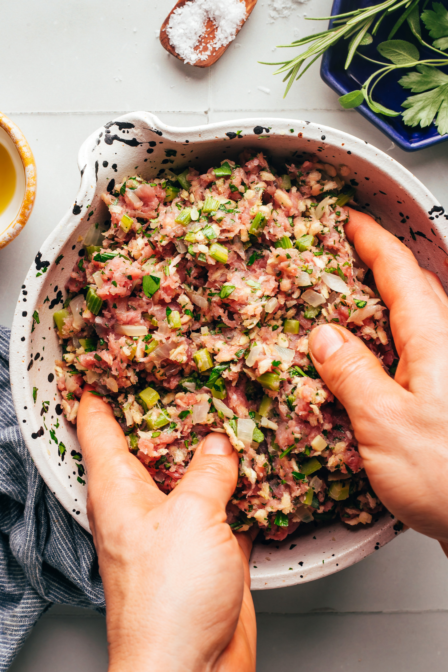 Mixing ground turkey in a bowl with sautéed vegetables and fresh chopped herbs