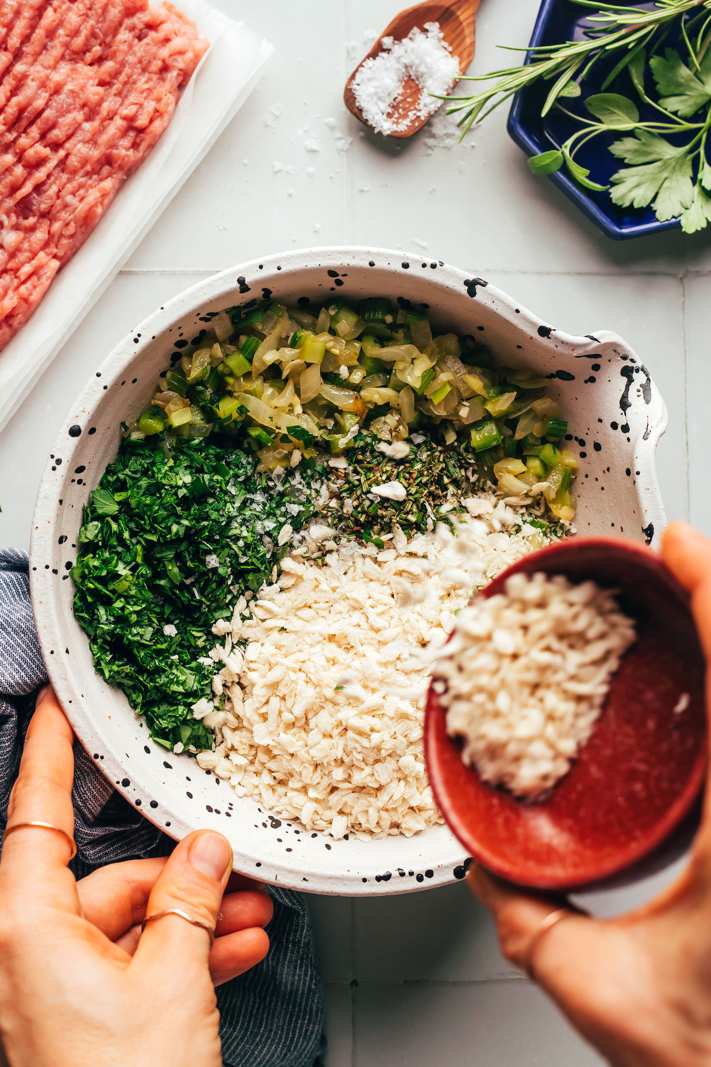 Adding breadcrumbs to a bowl with sautéed vegetables and chopped fresh herbs