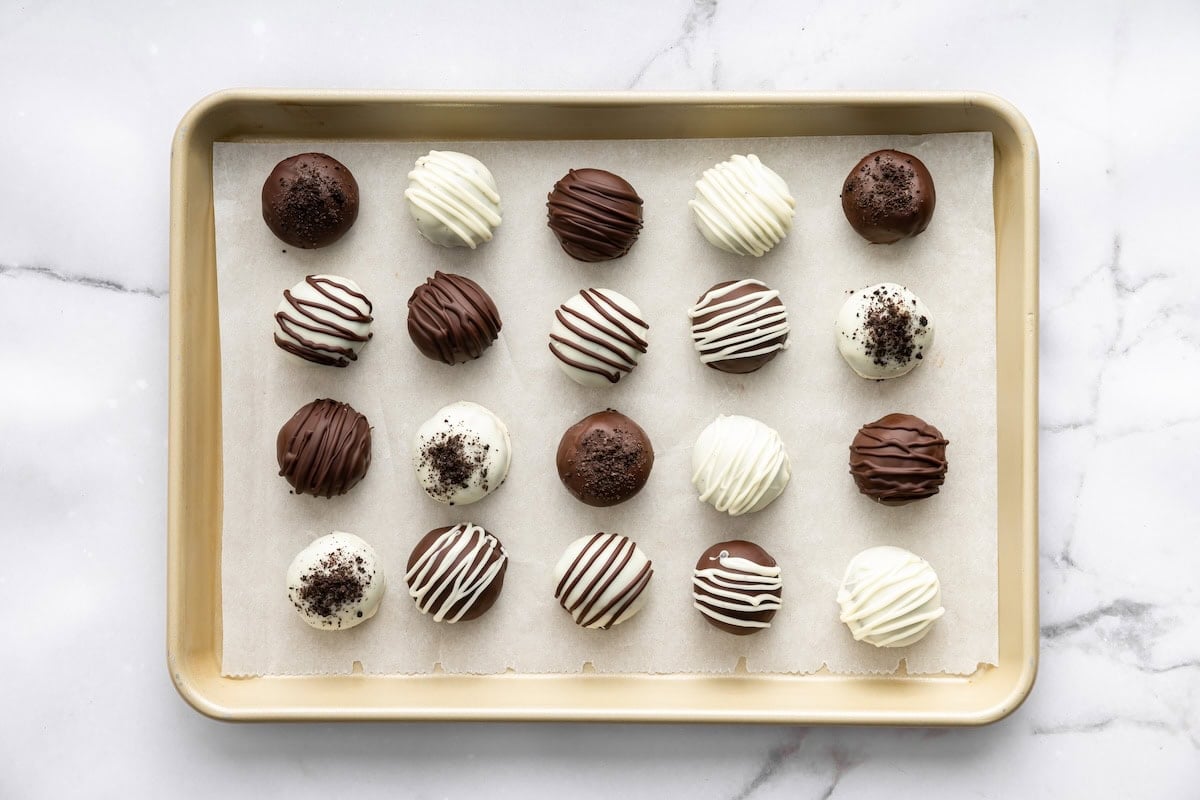 Rolled Oreo truffle balls arranged on a parchment-lined tray after coating in chocolate.