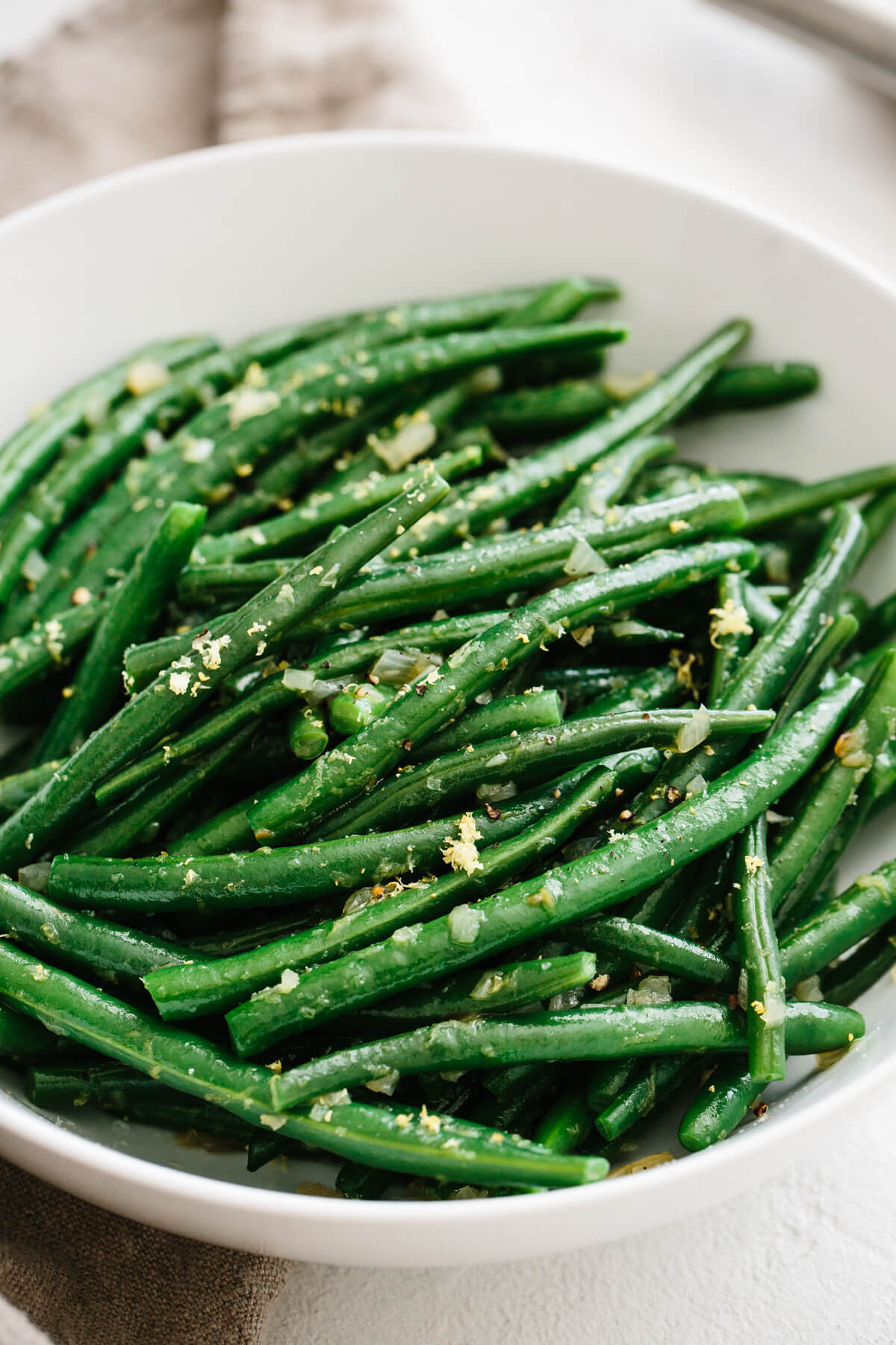 Green beans garnished with shallots and lemon in a white bowl.