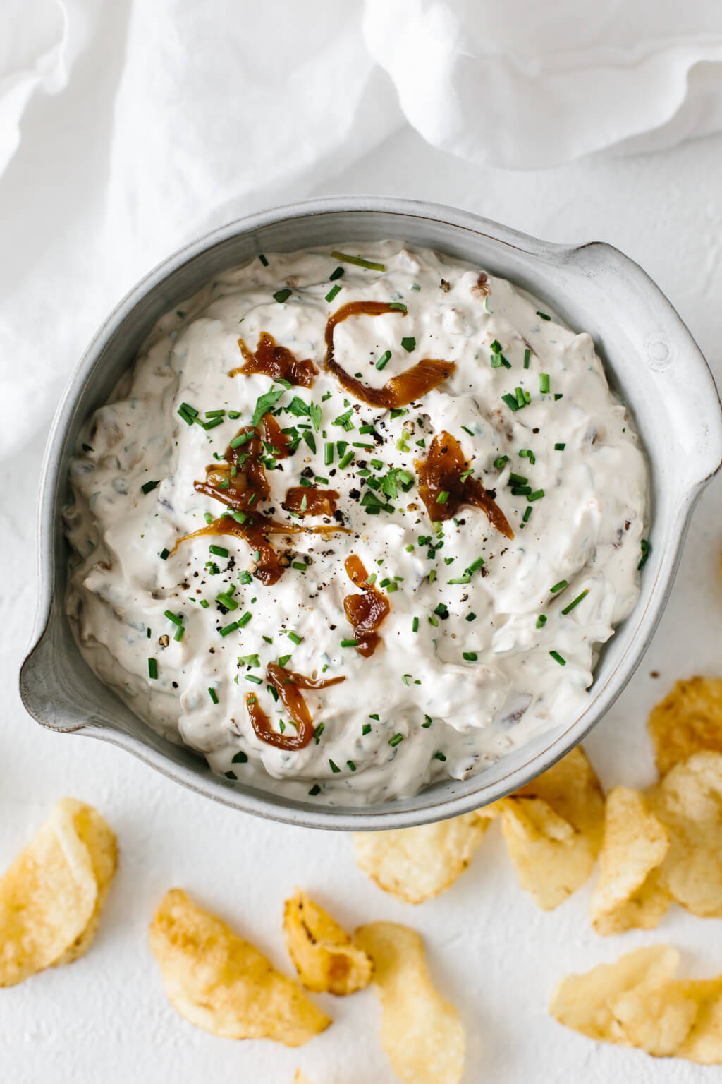 French onion dip in a ceramic bowl with potato chips next to it.