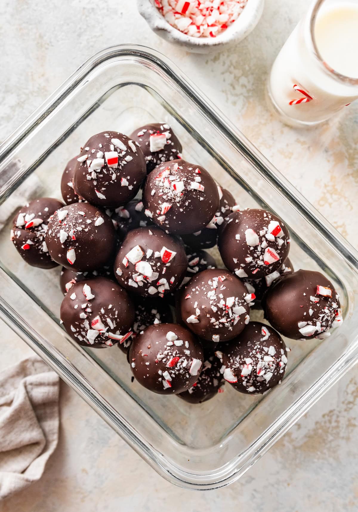 Glass container filled with finished chocolate peppermint protein balls with candy cane pieces.