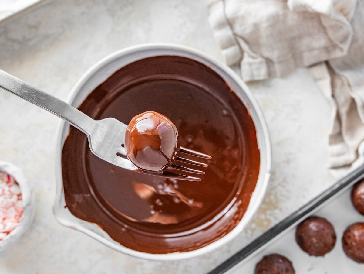 A fork dipping a protein ball into melted chocolate in a small bowl.