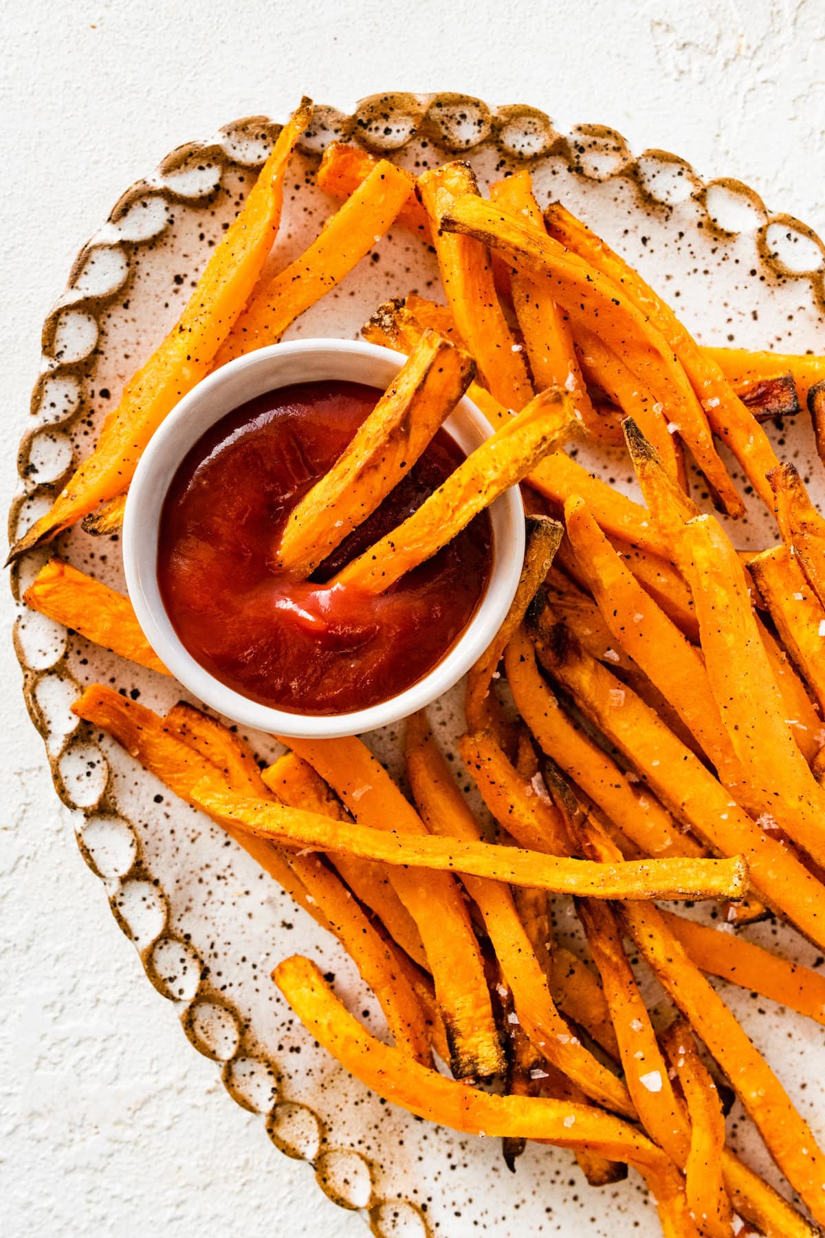 An overhead image of sweet potato fries on a white tray served alongside a small white bowl of ketchup. There are two fries dipped in the ketchup.