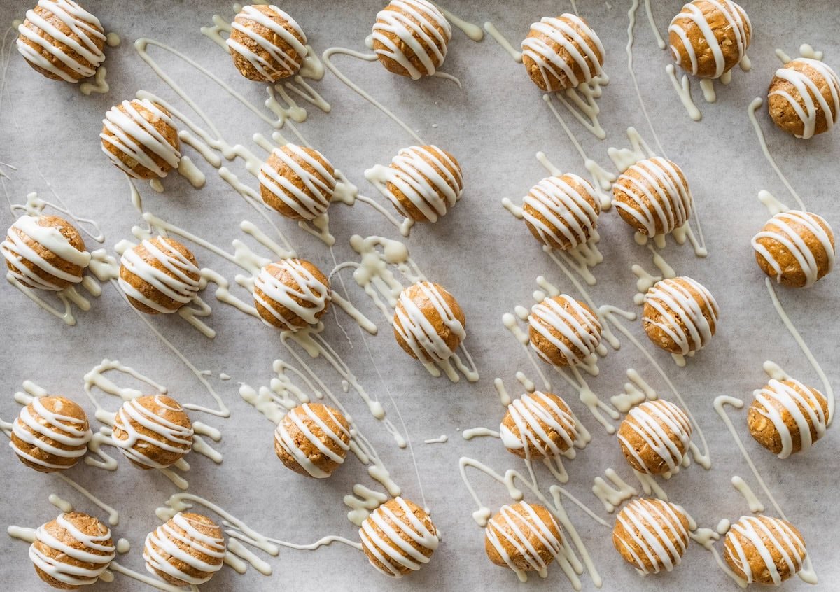 Gingerbread protein balls on a sheet pan drizzled with white chocolate and ready to chill.