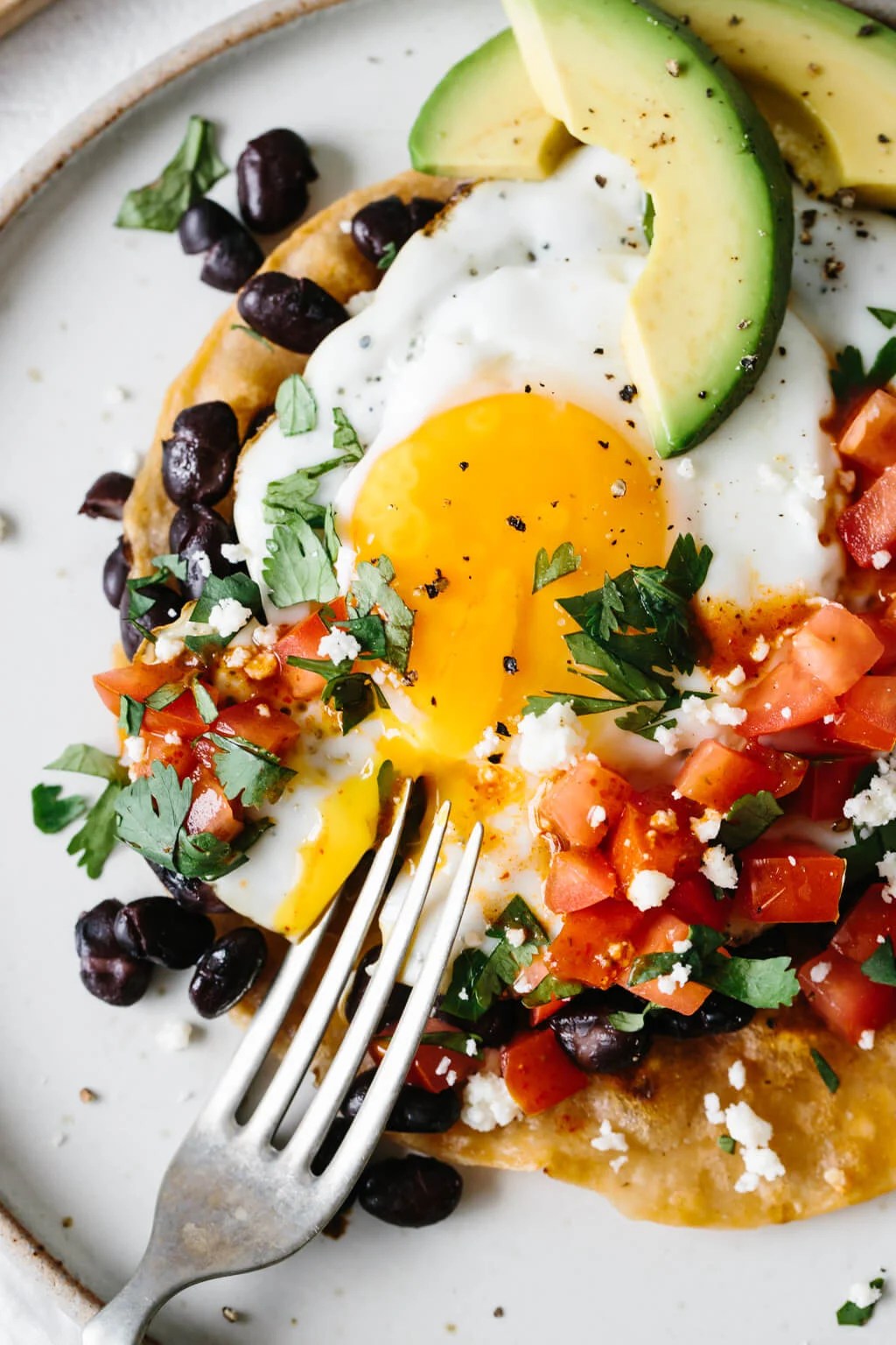 A fork broke open the yolk on a plate of huevos rancheros.