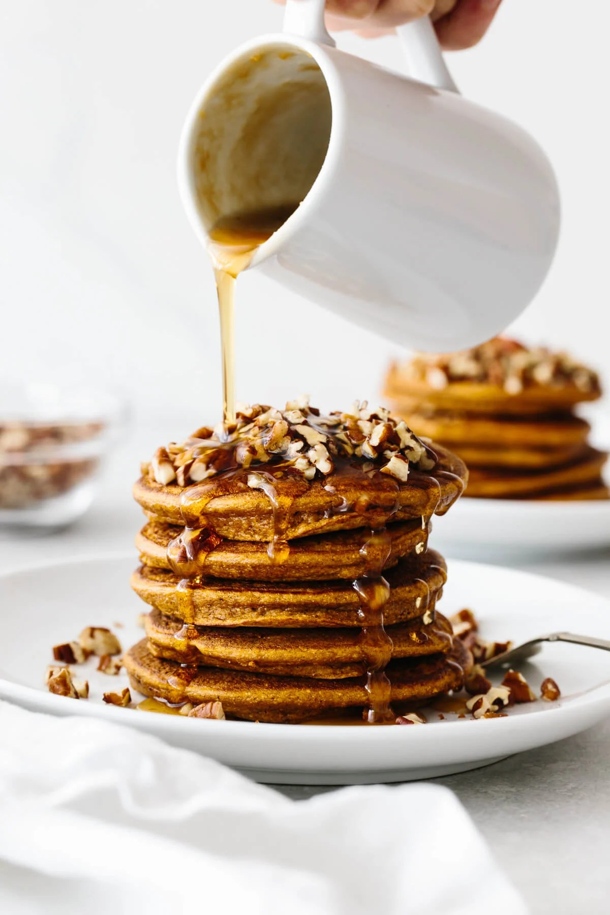 A stack of paleo pumpkin pancakes drizzled with maple ginger syrup.