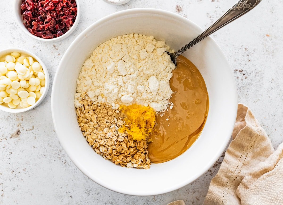 A mixing bowl with oats, protein powder, cashew butter, and orange zest used to make cranberry orange protein balls.
