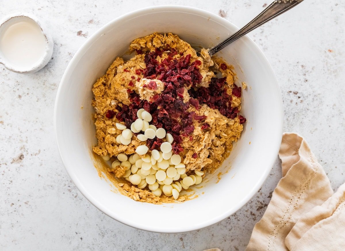 Dried cranberries and white chocolate chips added to a bowl of dough used to make cranberry orange protein balls.