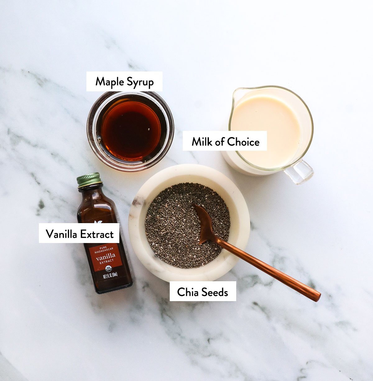 chia seeds, milk, maple syrup, and vanilla labeled on a white surface. 