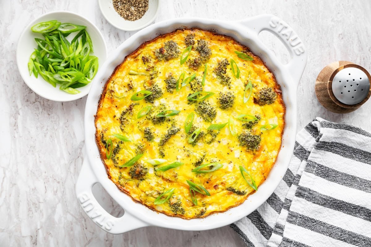 A crustless quiche with broccoli, ham, onion, and cheese in a round baking dish after being baked.