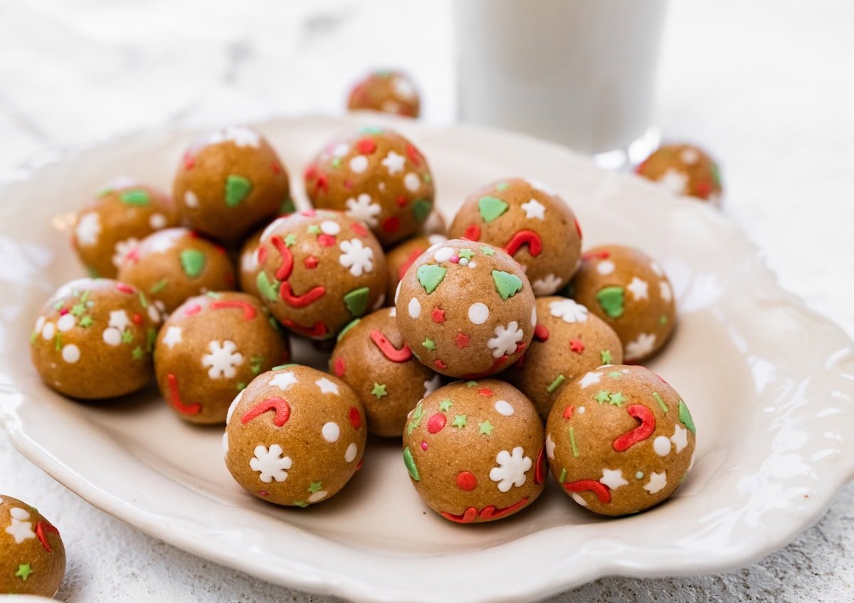 A cream-colored plate piled with sugar cookie protein balls decorated with festive sprinkles.