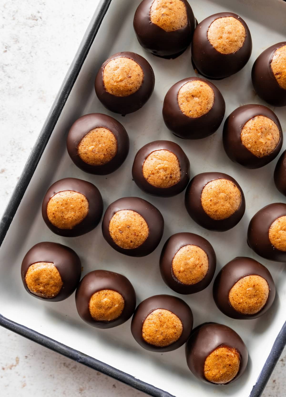 Chilled buckeye balls coated in dark chocolate and arranged neatly on a parchment-lined pan.
