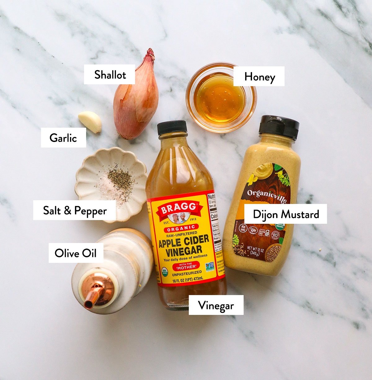 vinegar, dijon dressing, olive oil, shallot, garlic, honey, and spices labeled on a white surface. 