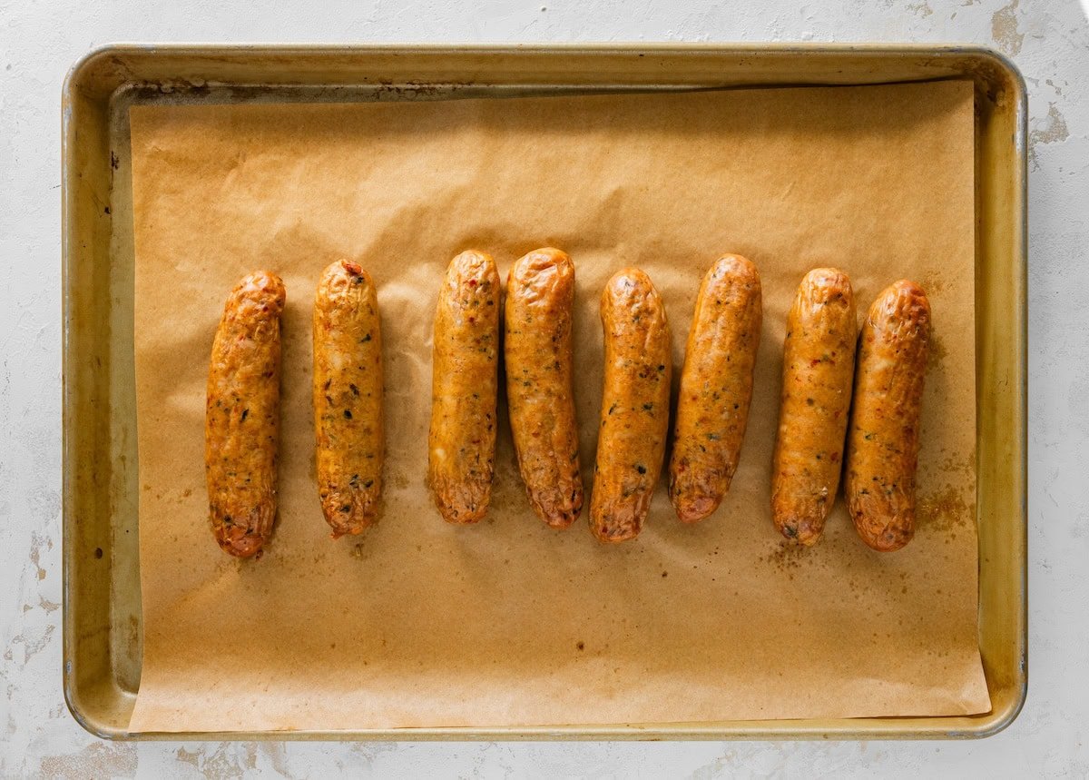 Cooked chicken sausage links arranged on a parchment lined sheet pan.