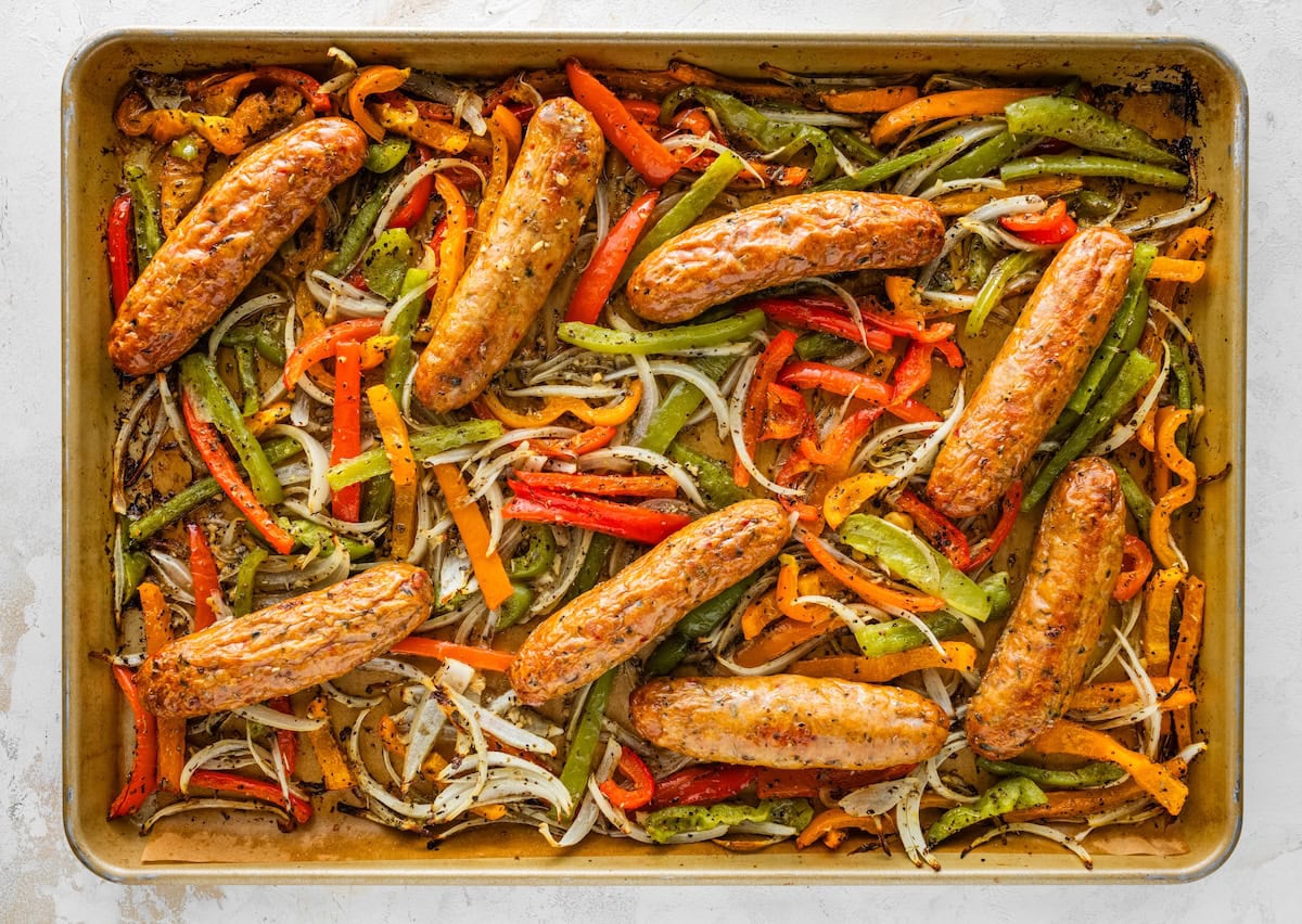 Chicken sausage and sliced peppers and onions roasting together on a sheet pan.