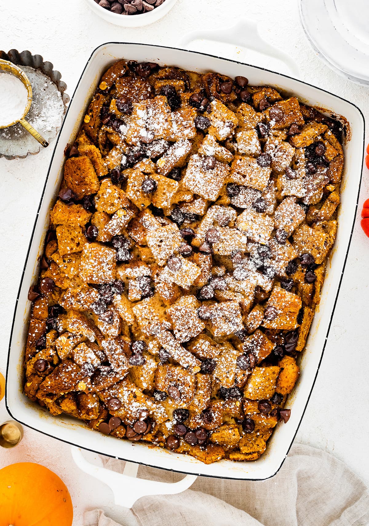 Pumpkin French Toast Casserole in a square baking dish topped with powdered sugar and chocolate chips.