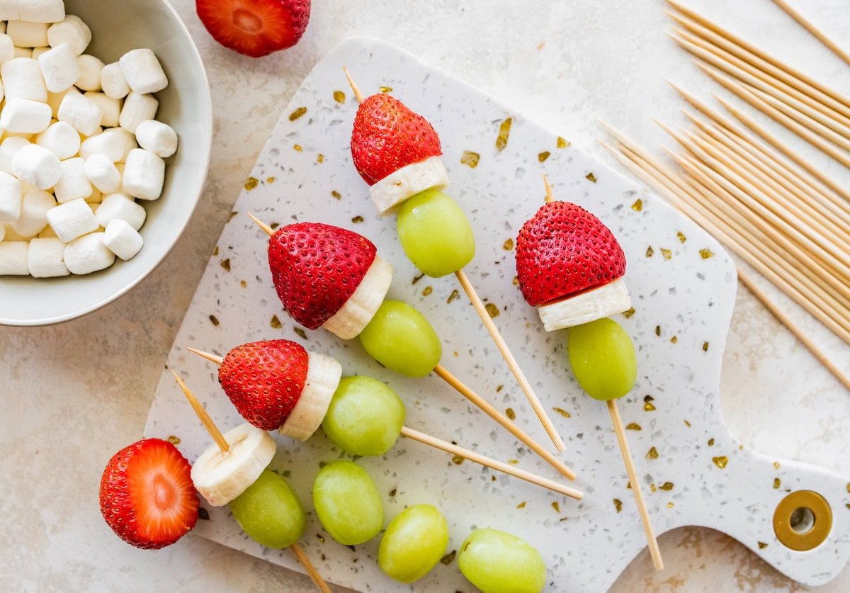 Assembled Grinch fruit kabobs on parchment paper with strawberries, bananas and grapes.