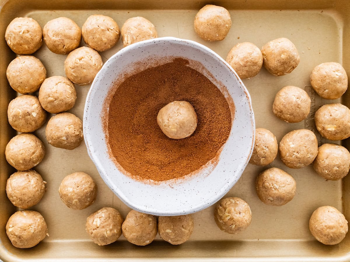 Protein ball being rolled in mixture Protein ball being rolled in a cinnamon sugar mixture on a sheet pan with more balls around.