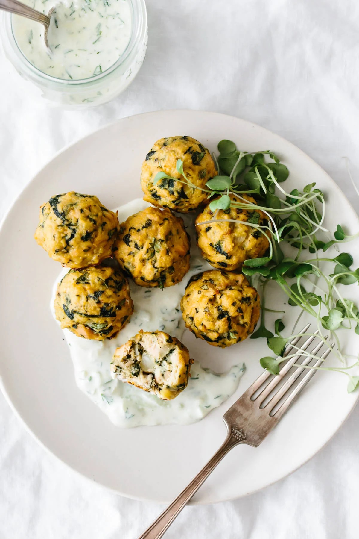 Tuna meatballs on a plate with tzatziki sauce and micro greens.