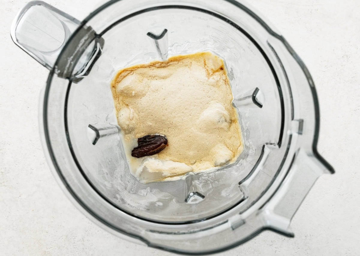 Blender filled with shake ingredients including ice, almond butter and a medjool date before blending.