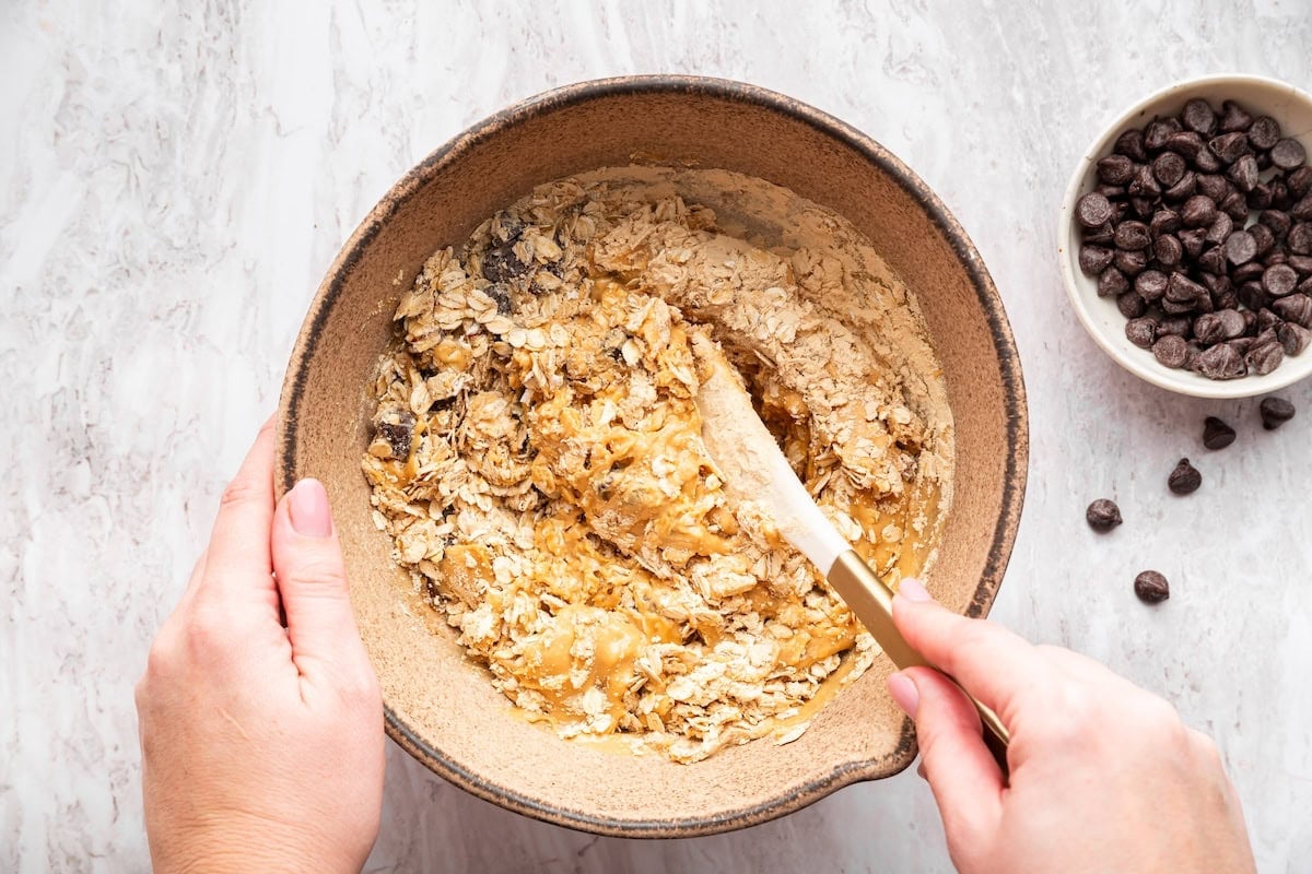 Mixing bowl with oats, peanut butter and chocolate chips being stirred together.