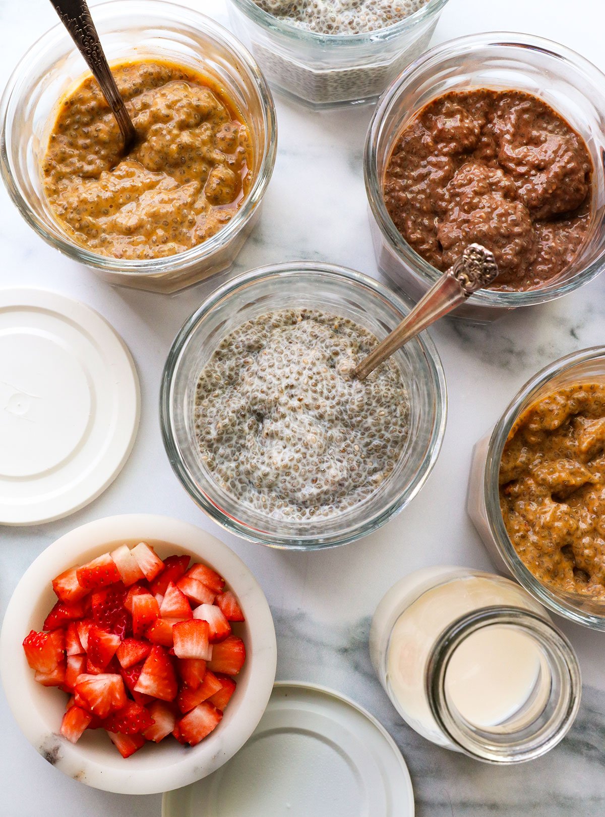 thickened chia pudding in glass jars with 3 flavors nearby. 