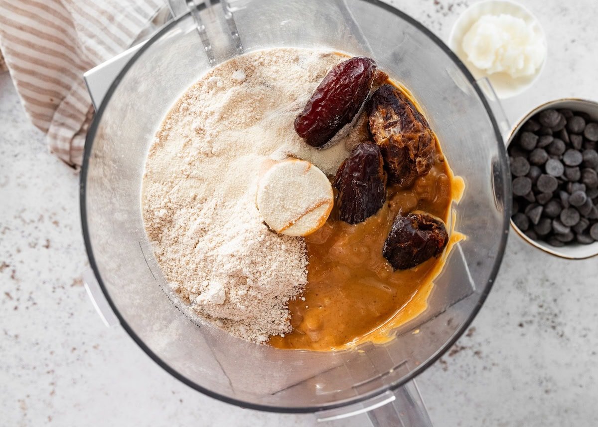 Dates, oat flour, protein powder and peanut butter added to a food processor before blending.