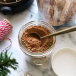 hot chocolate mix with a tablespoon in a glass jar with ribbon nearby.