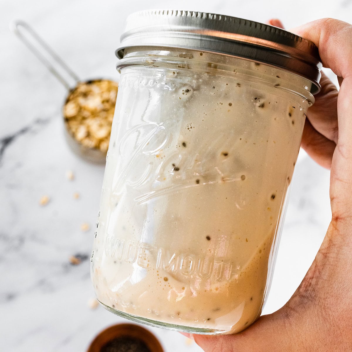 A woman's hand holding a mason jar with a lid with overnight oats.