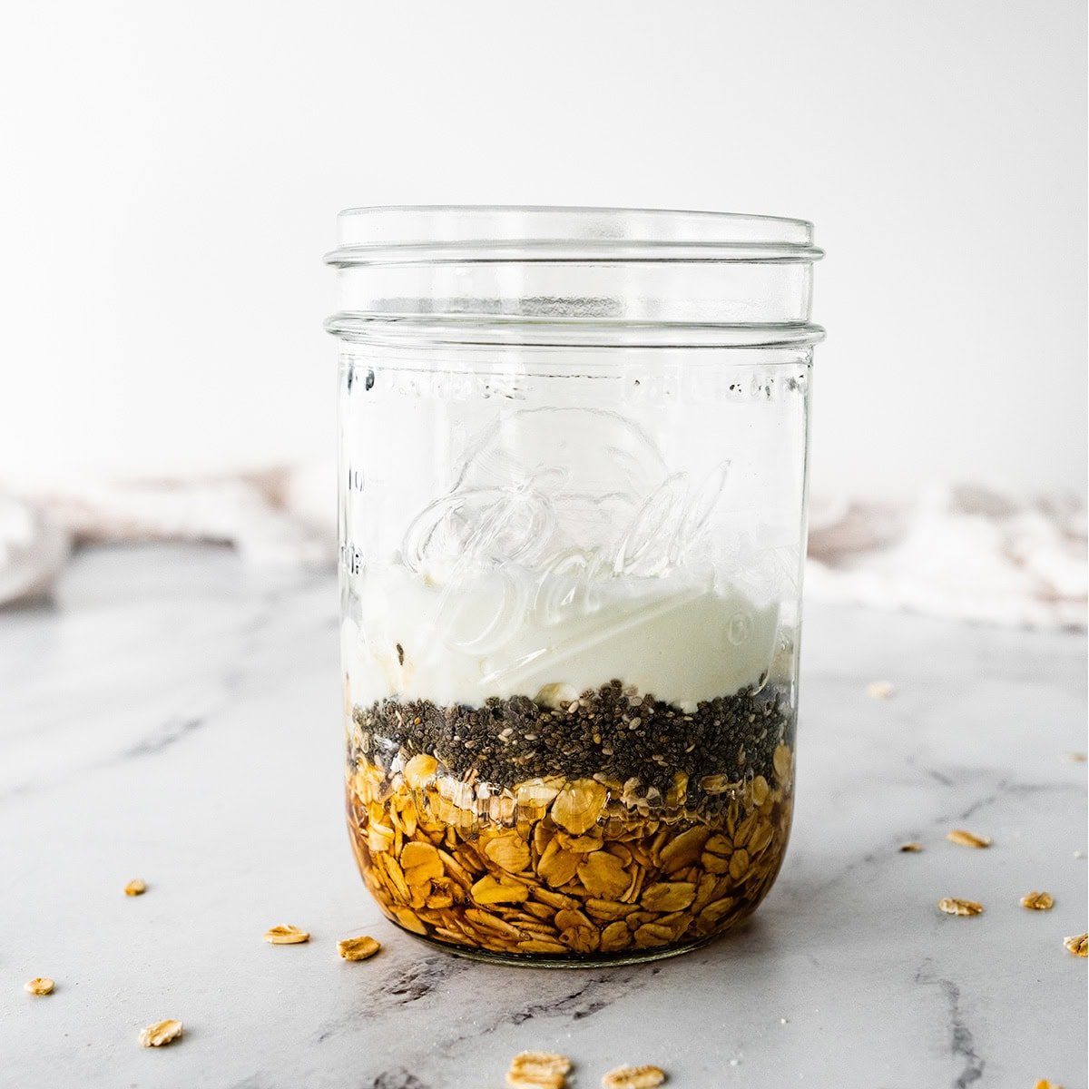 Oats, chia seeds, maple syrup and yogurt layered in a mason jar for overnight oats.