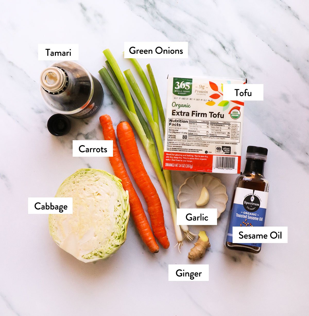 cabbage, carrots, green onions, tamari, tofu, and sesame oil labeled on a white surface. 