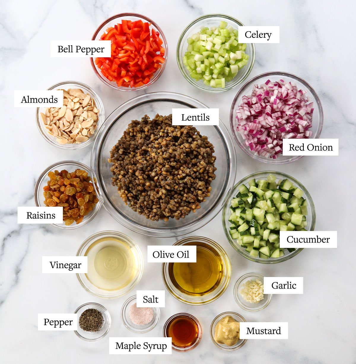 Lentil salad ingredients labeled in glass bowls on a white surface.