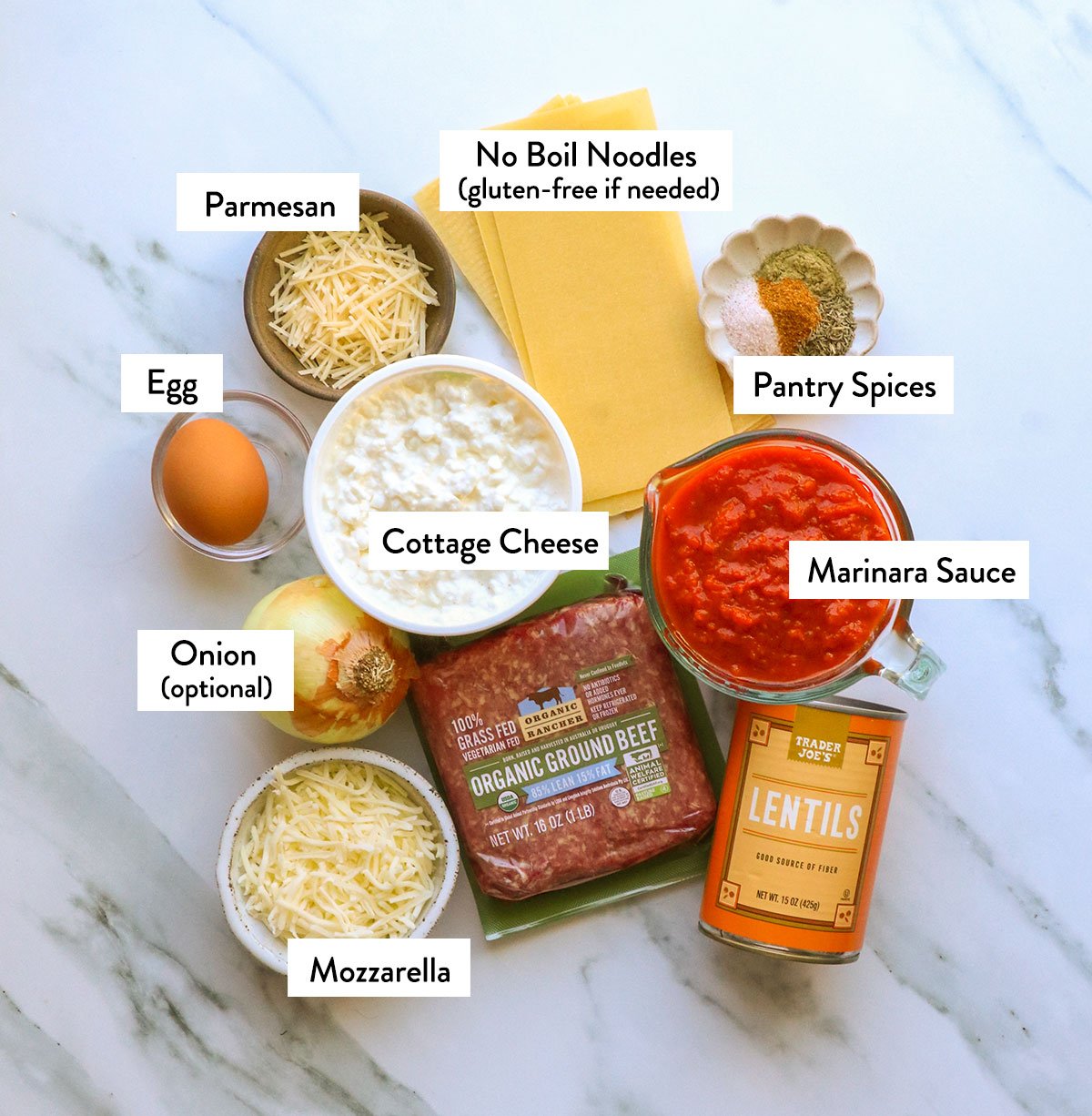 ground beef, cottage cheese, lasagna noodles, sauce, lentils, egg, and spices labeled on a white surface. 