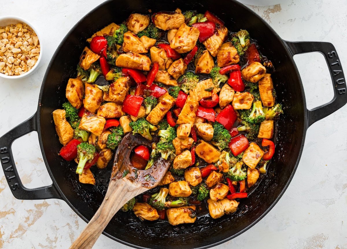 Kung pao chicken with bell peppers and broccoli cooking in a skillet