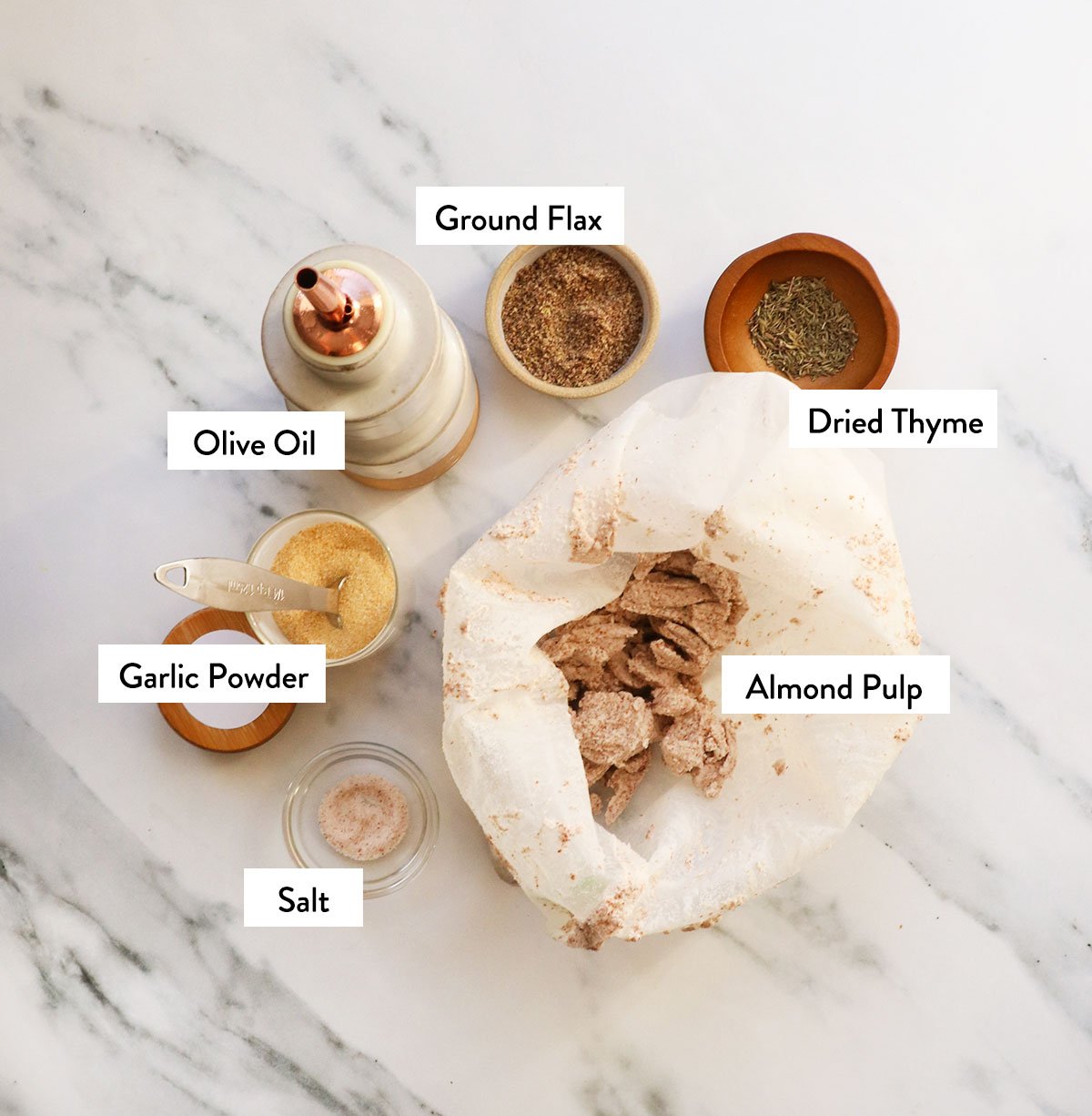 almond pulp, olive oil, spices, and ground flax labeled in bowls. 