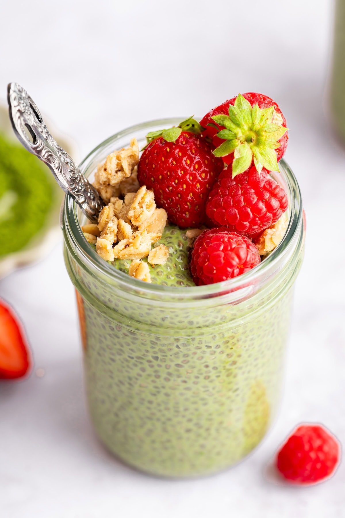 Single jar of matcha chia pudding topped with strawberries and granola ready to eat.