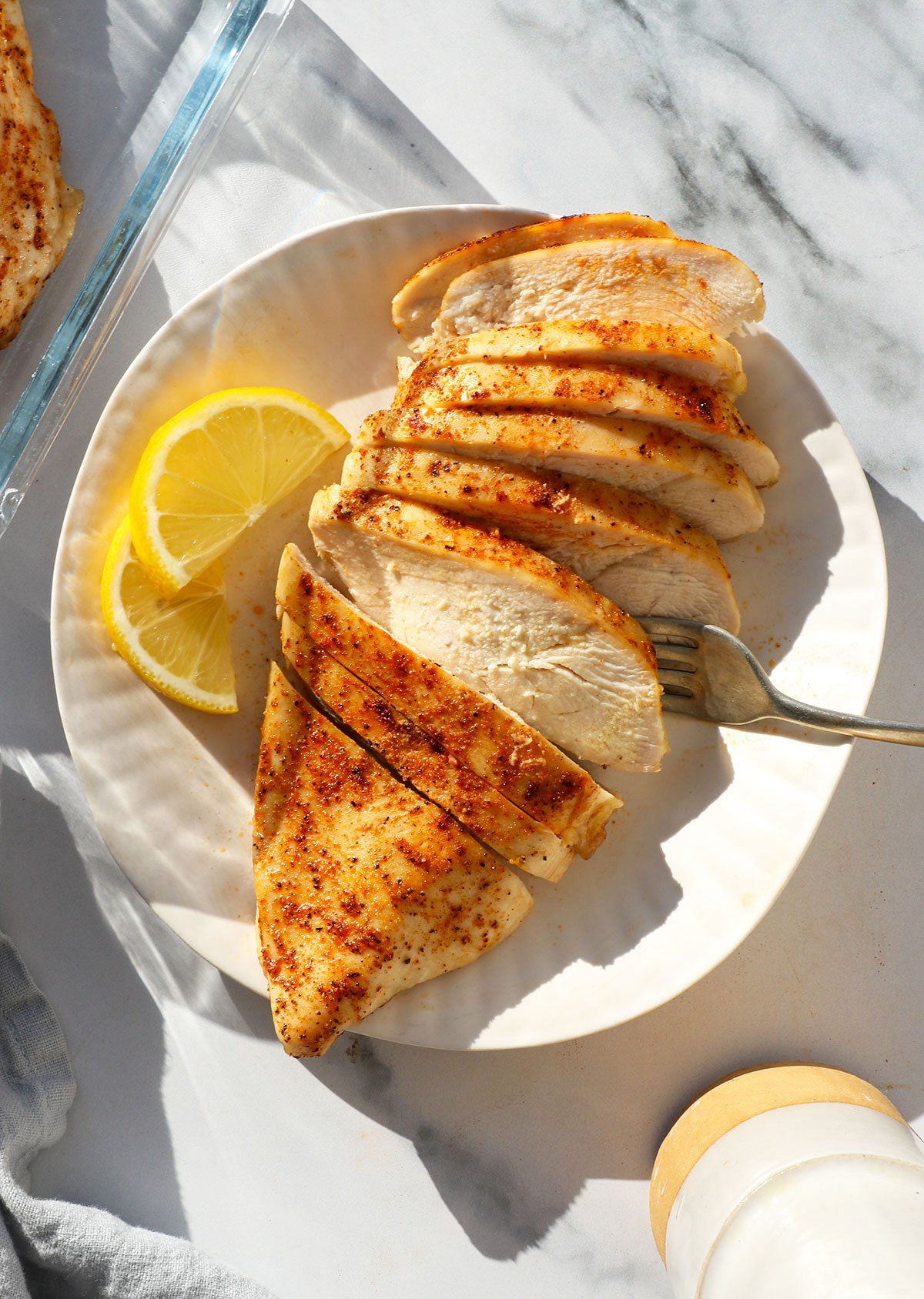 baked chicken breast sliced on a white plate with lemon slices nearby. 