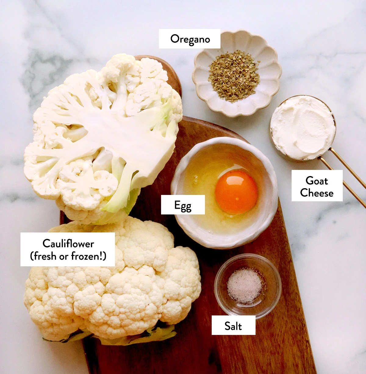 cauliflower cut in half, plus an egg, goat cheese, and spices labeled on a cutting board. 