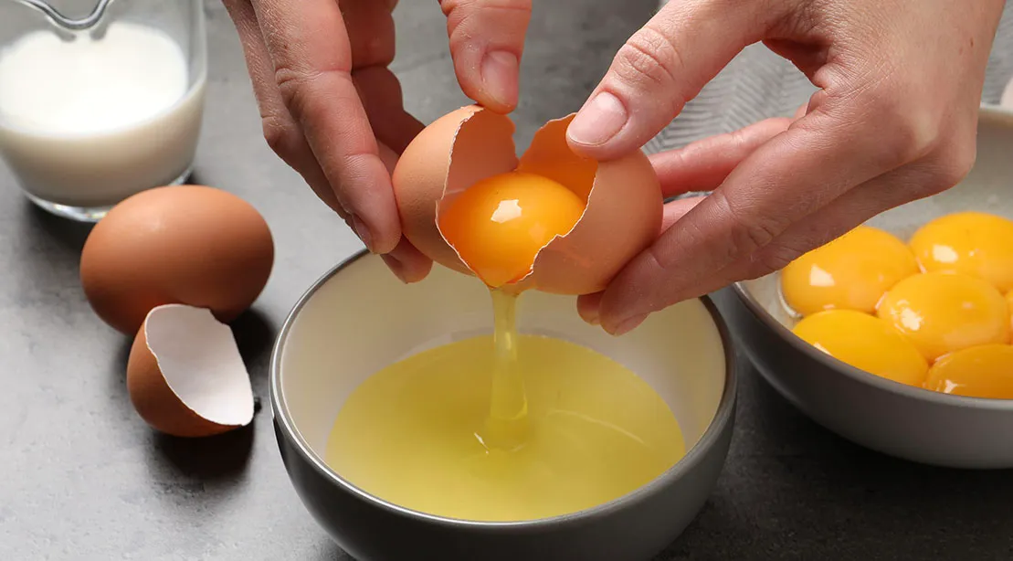 Hands cracking a whole egg and separating the egg whites