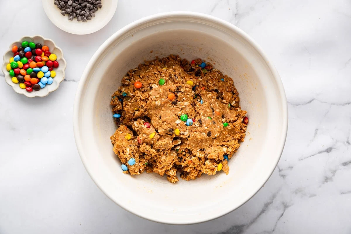 Monster cookie protein ball dough mixed in a bowl with oats, chocolate chips, and M&M’s.