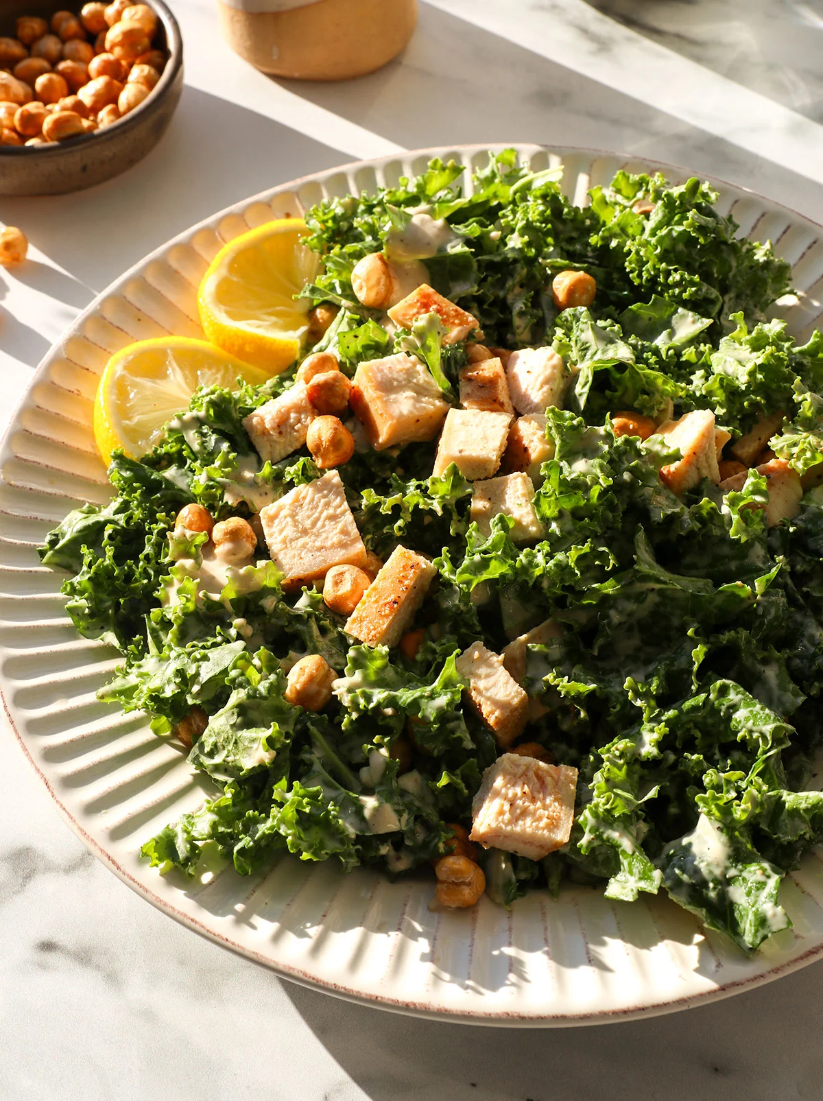 kale salad on a plate with tahini dressing and chicken. 