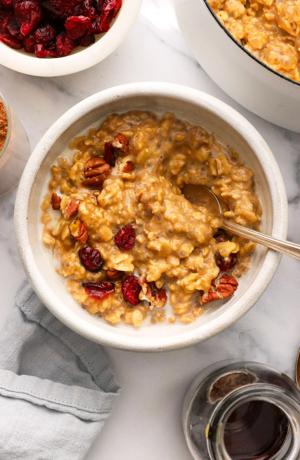 pumpkin oatmeal stirred with cranberries and pecans in a white bowl. 