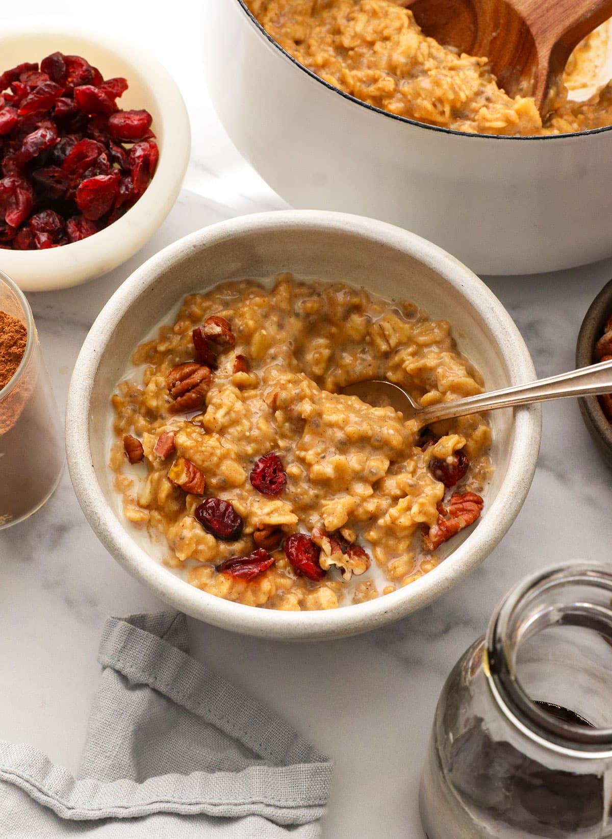 angled view of pumpkin oatmeal in a white bowl with cranberries, pecans, and extra milk. 