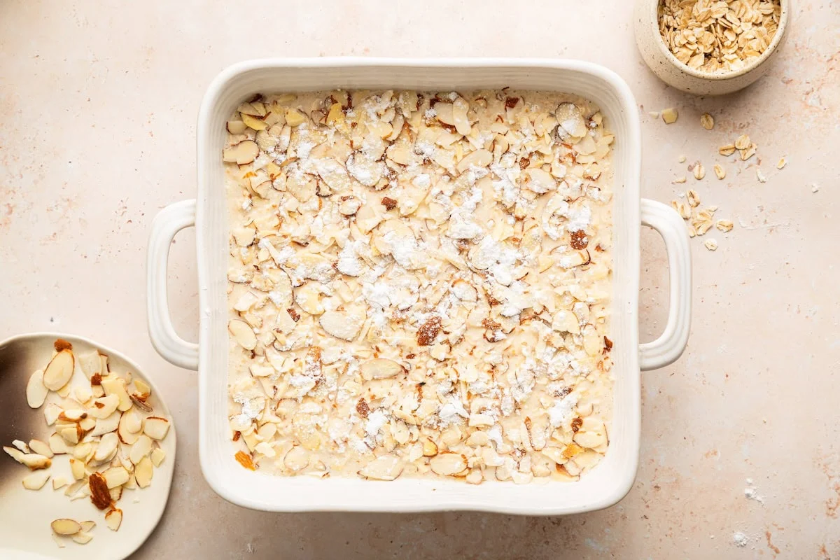 Unbaked almond croissant baked oatmeal with sliced almonds in baking dish.