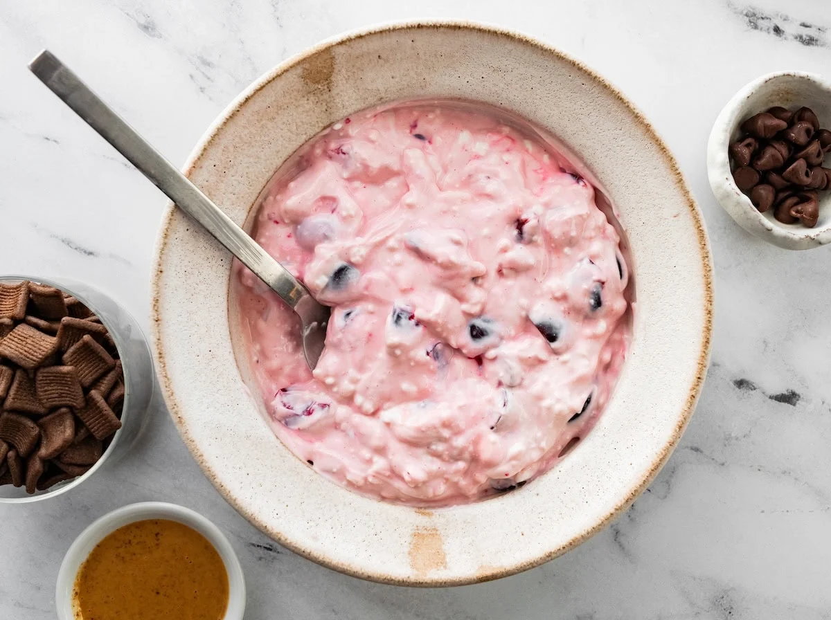 Cherry yogurt and cottage cheese mixture stirred together in bowl.