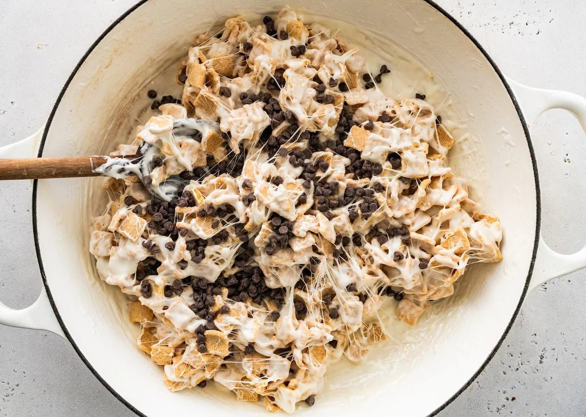 A mixture of melted marshmallows, cereal, and mini chocolate chips in a large pot.