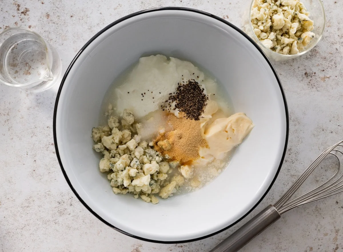 A large mixing bowl of crumbled blue cheese, mayonnaise, greek yogurt, white vinegar, and spices used to make a dressing.