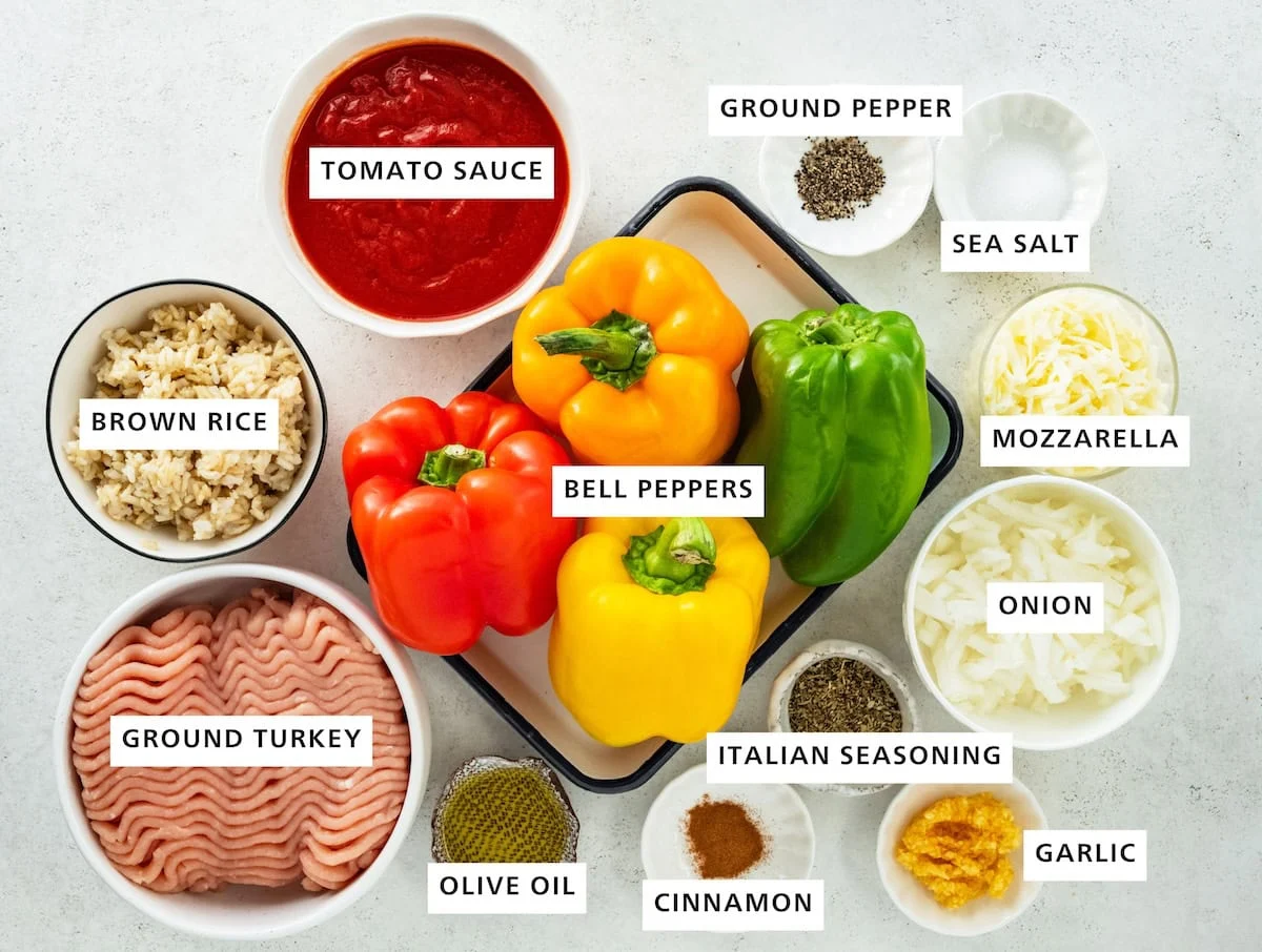 Ingredients for turkey stuffed peppers including bell peppers, ground turkey, grown rice, tomato sauce, ground pepper, sea salt, mozzarella, onion, italian seasoning, garlic, cinnamon, and olive oil.