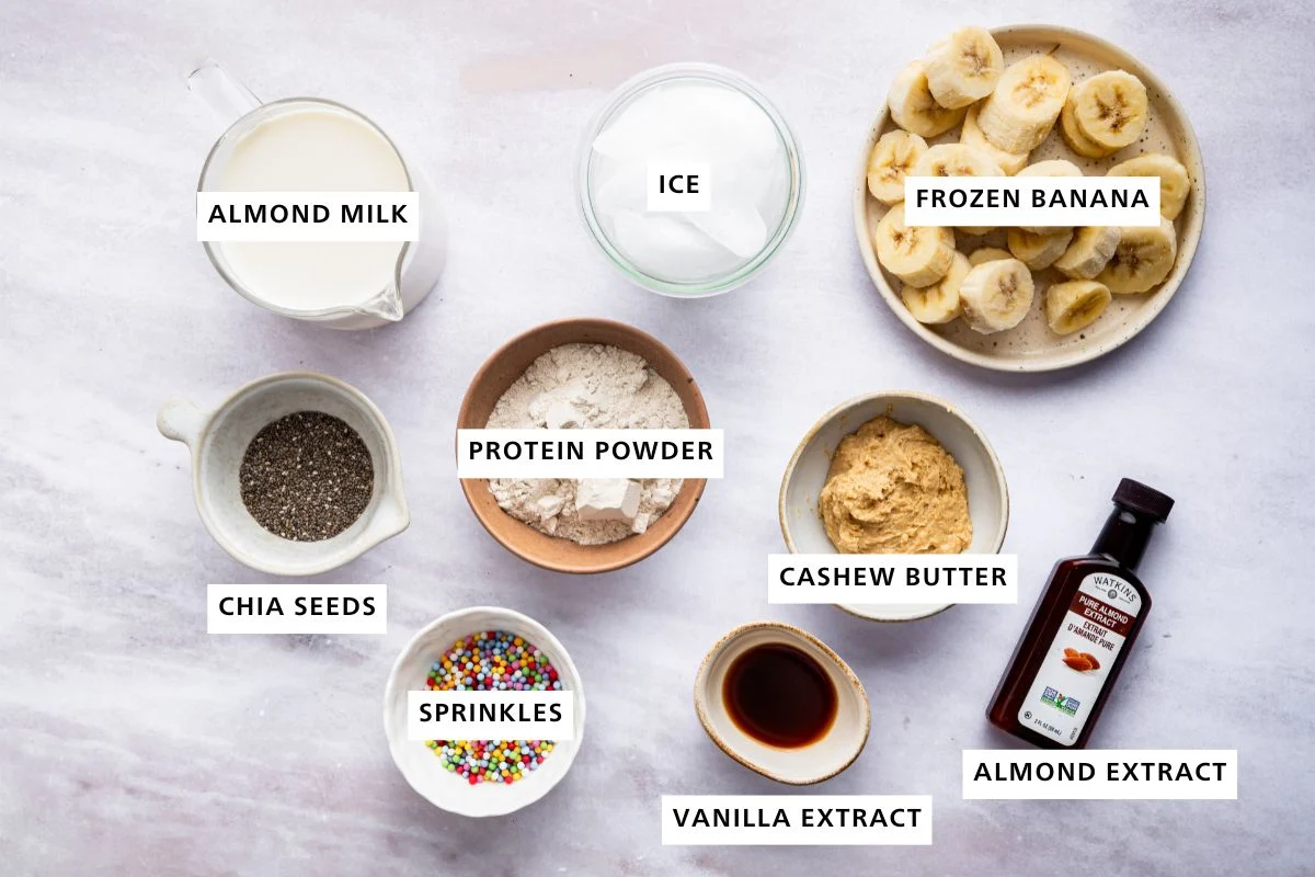 Ingredients for the cake batter protein shake: almond milk, ice, frozen banana, chia seeds, protein powder, cashew butter, sprinkles, vanilla and almond extract.